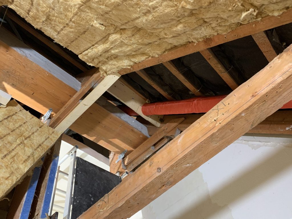 Detailansicht der Dachkonstruktion mit Dämmwolle, Holzsparren und rotem Isolierrohr.