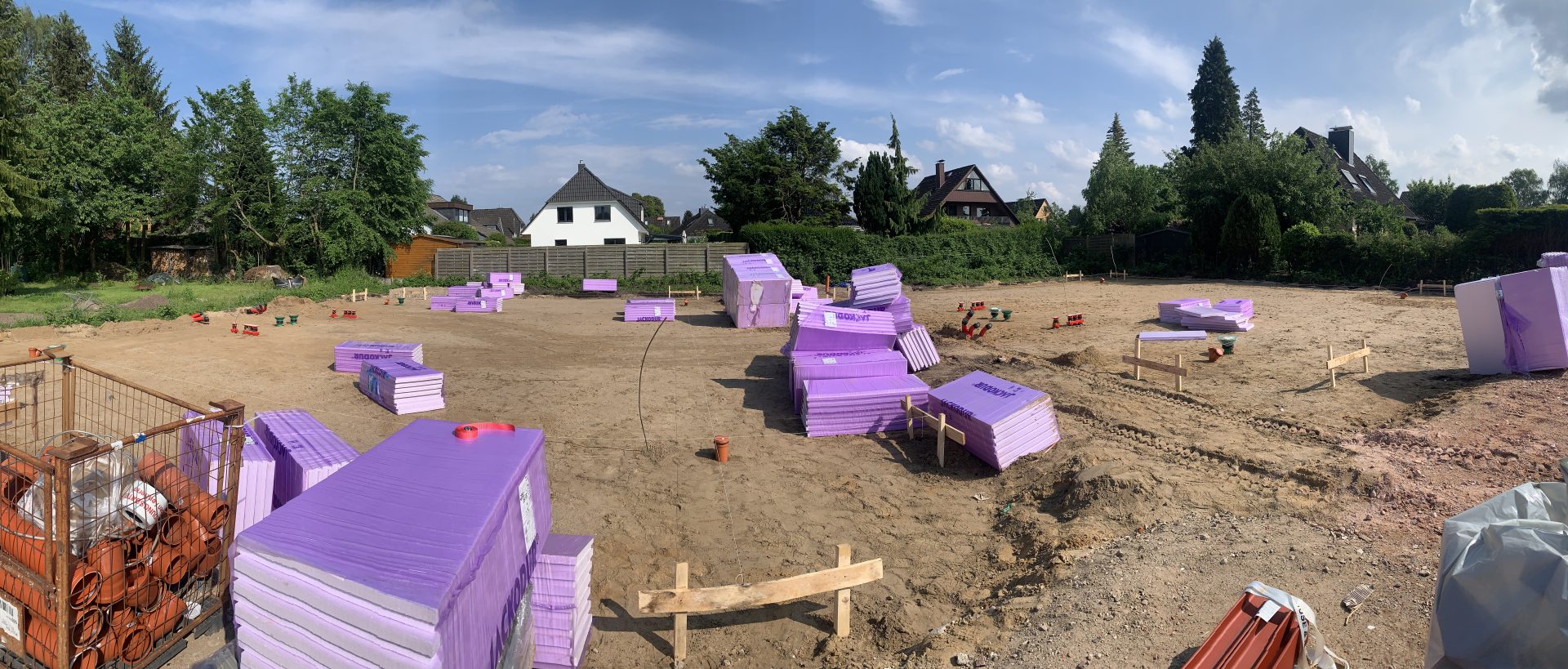 Panoramaaufnahme einer Baustelle mit gelagerten Dämmplatten aus XPS/EPS auf dem Erdreich.