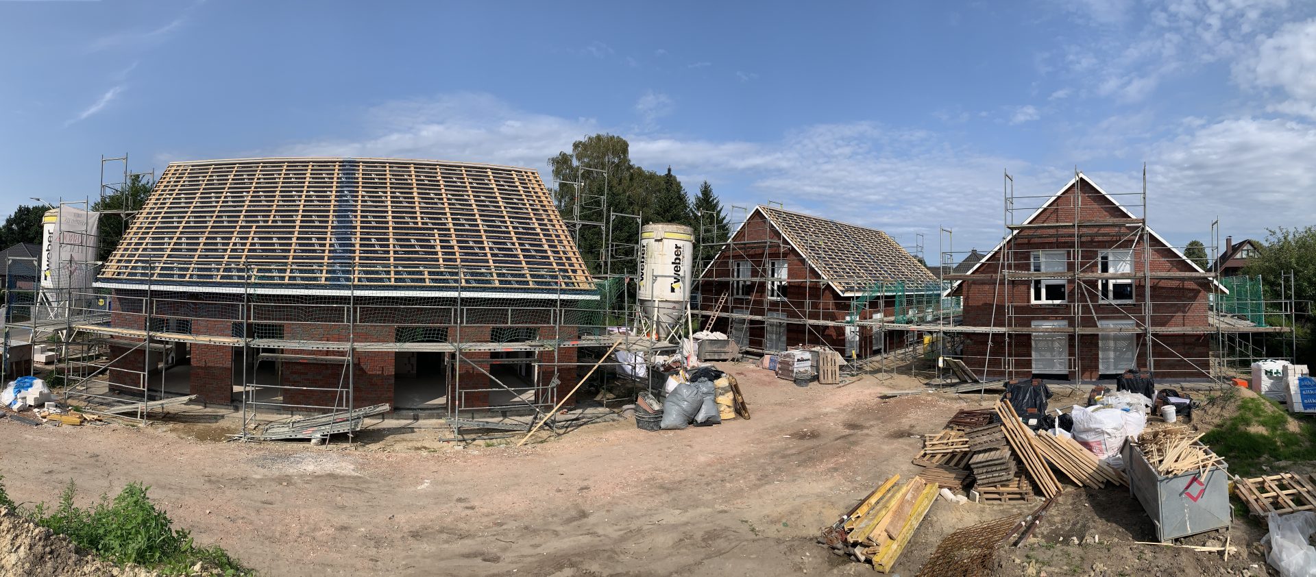Panoramaaufnahme einer Baustelle mit mehreren eingerüsteten Ein- und Zweifamilienhäusern im Klinkerbau.