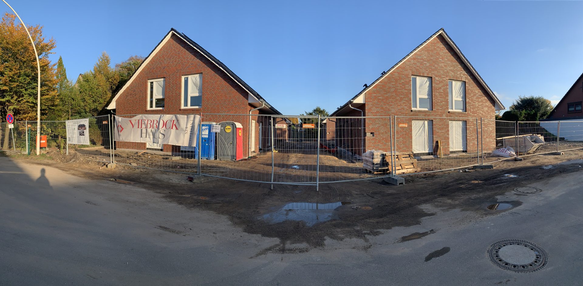 Panoramaansicht von zwei im Bau befindlichen Klinker-Wohnhäusern hinter einem Bauzaun.