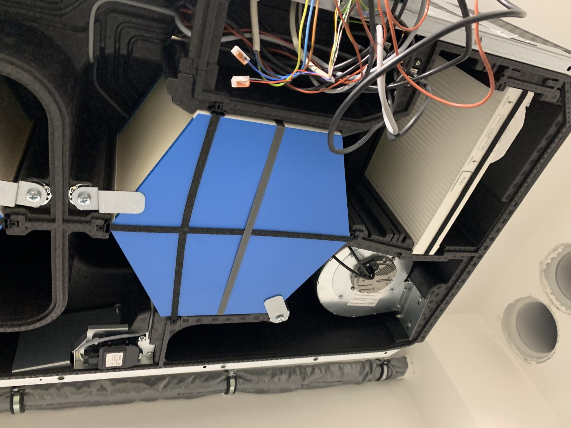 Offene Gehäuseansicht einer Lüftungsanlage mit Wärmetauscher, Filter, Lüftermotor und Verkabelung.